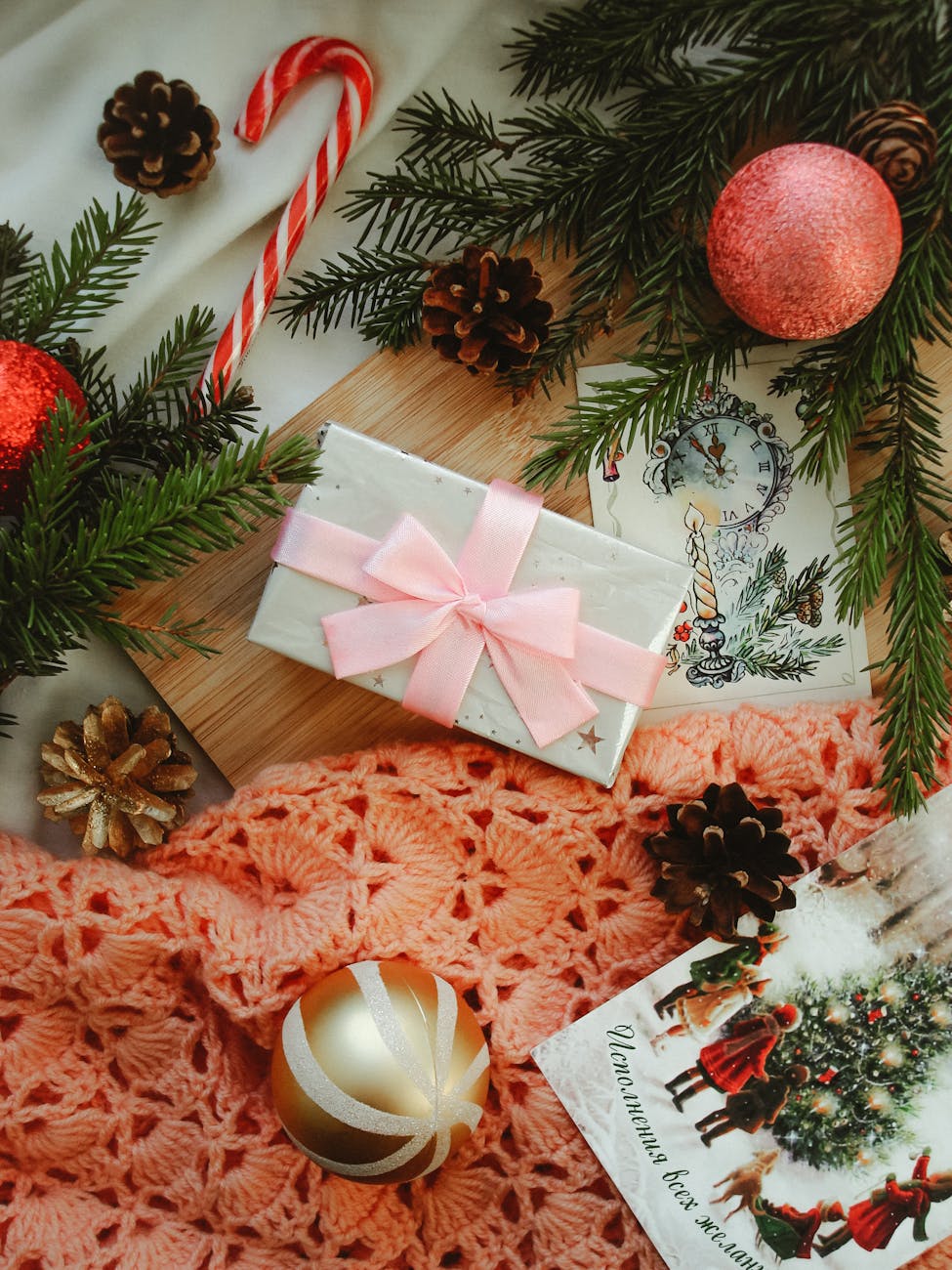 A cozy flatlay with Christmas decorations, a gift box, pine cones, and candy cane on wooden surface.