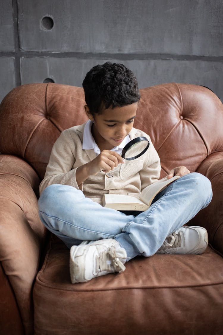 Positive Little Arabian Boy Reading Interesting Book With Magnifying Glass