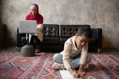 Arabian mother in hijab working with laptop while son writing