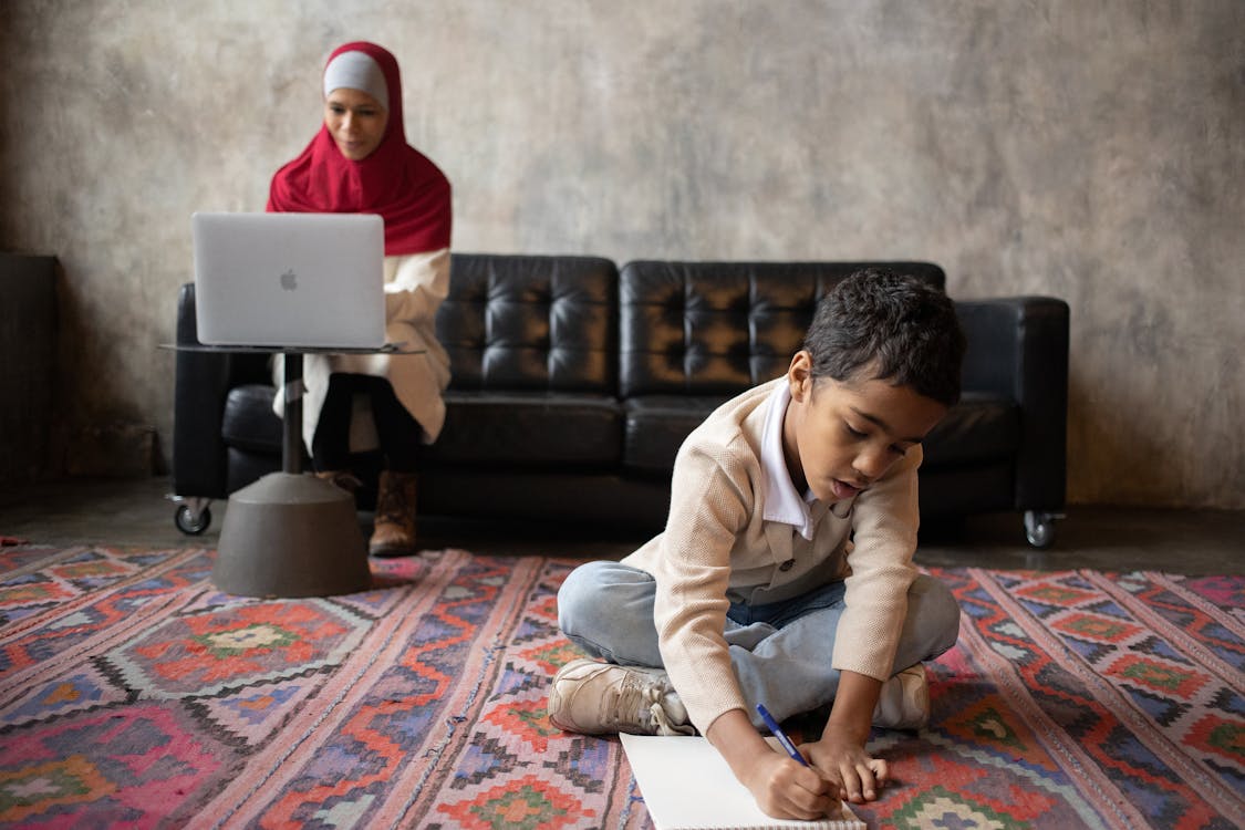 Arabian mother in hijab working with laptop while son writing