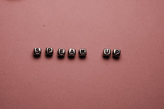 Close-up of beads spelling 'Speak Up' on a pink background, encouraging self-expression.