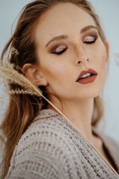Close-up portrait of a woman in knitted dress with glamorous makeup and closed eyes.