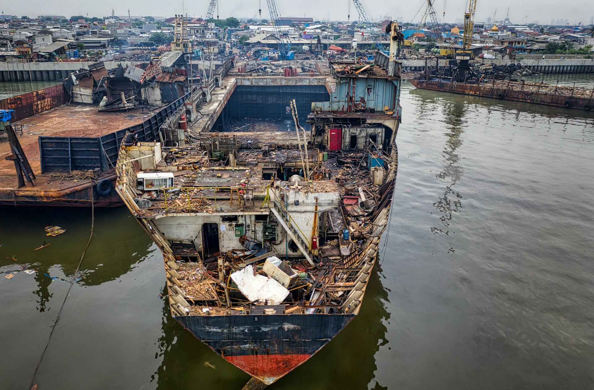 From above of aged rusty ship with rubbish moored in abandoned port in cloudy day in daylight