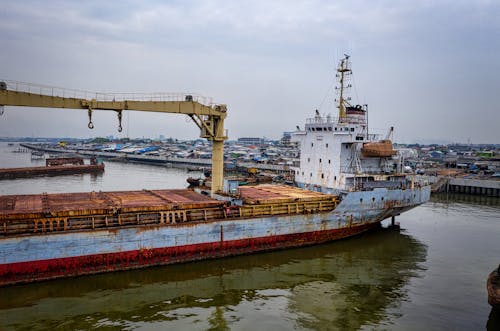 Aged cargo vessel moored in port in calm water under cloudy sky in daytime
