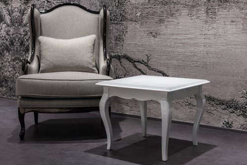 Vintage interior with gray armchair placed near white table on dark floor near wall