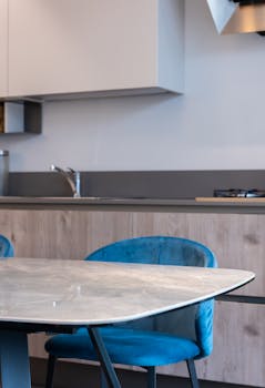 Interior of modern kitchen with chairs and table near cabinet and kitchenware with sink