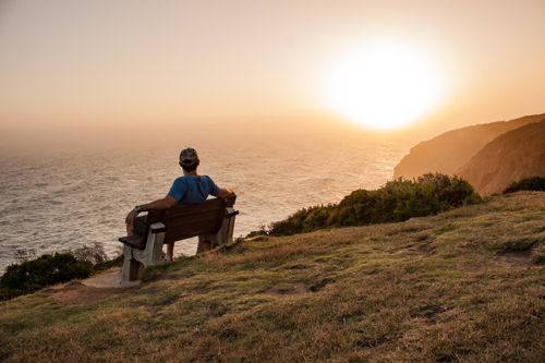 Free A man sitting on a bench overlooking the ocean at sunset, creating a tranquil scene. Stock Photo