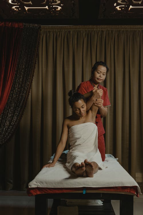 A Woman in Red Clothes Massaging a Woman Sitting on Massage Bed