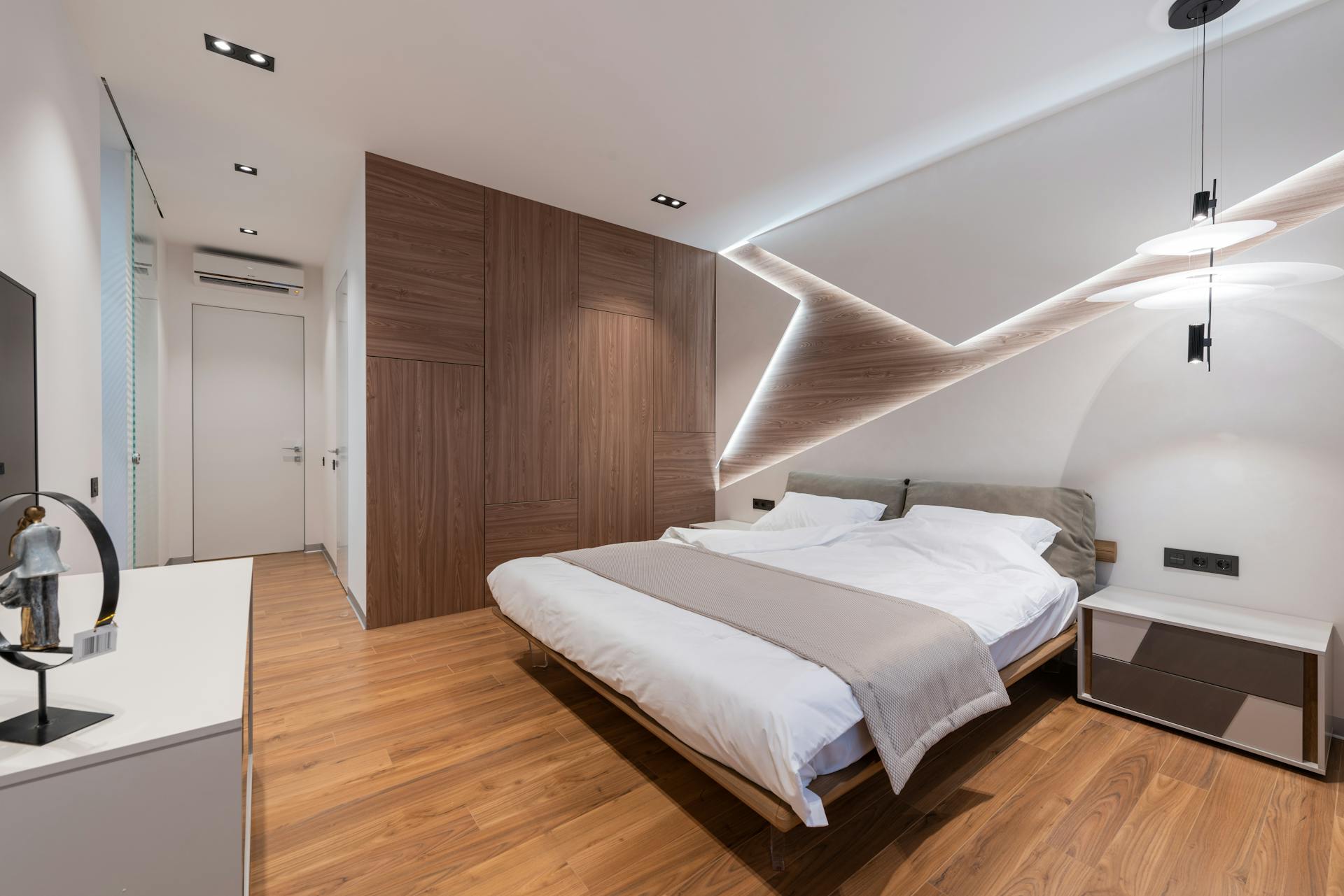 Light modern hotel room interior with soft white bed and wooden floor near cupboard