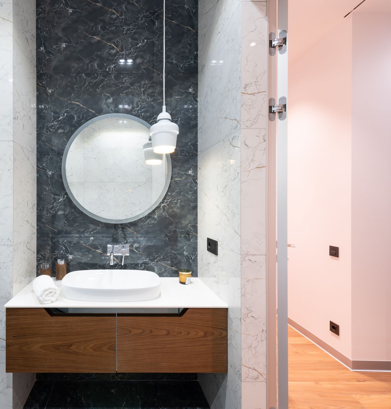 Small white pendant light hanging beside a round mirror over a vanity in a black marble bathroom