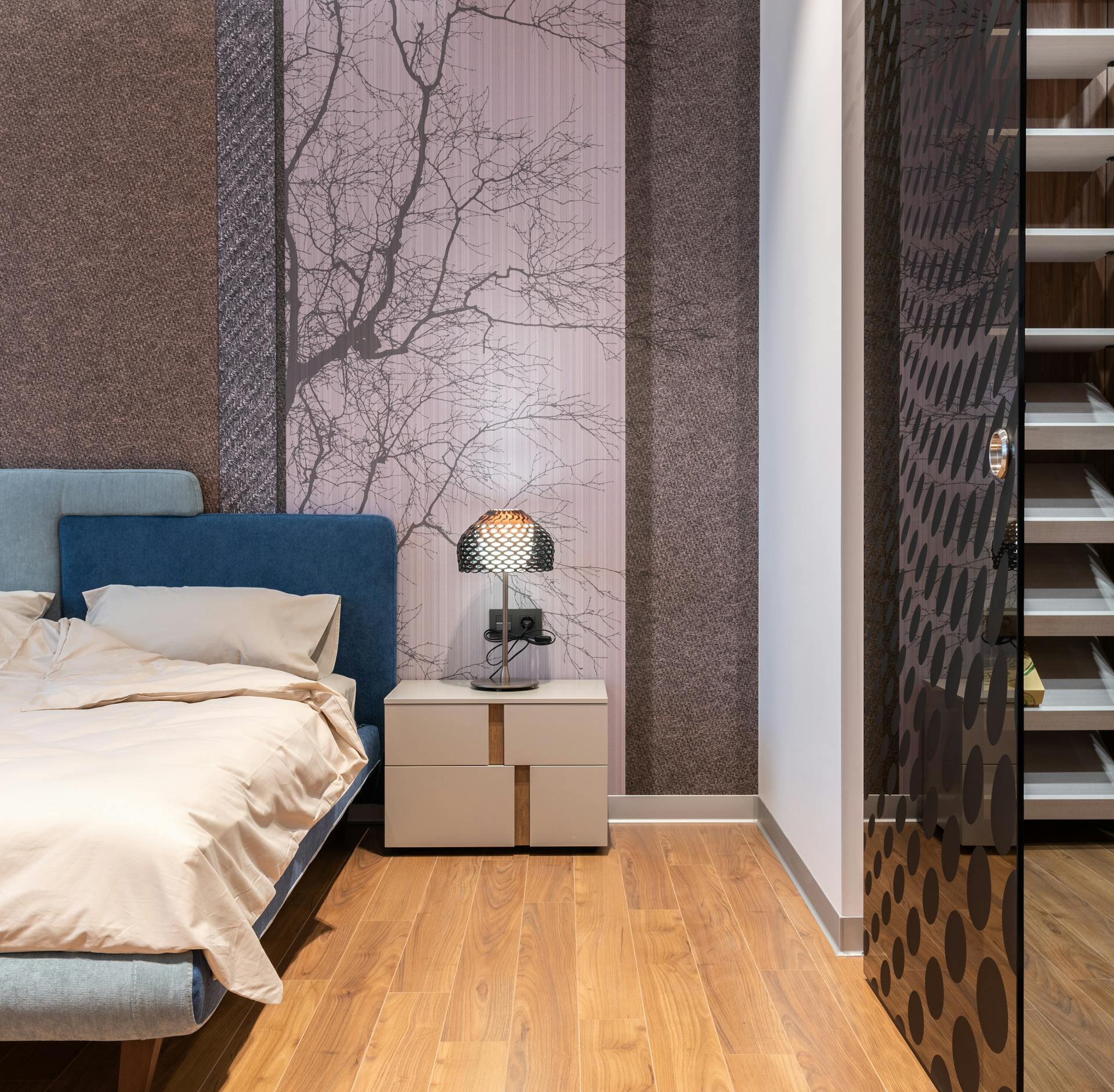 Contemporary light room interior with bed near table with lamp near wall and glass entrance on wooden floor