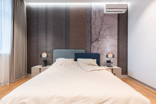 Interior of modern bright room with bed near table with lamp near wall and window with curtains and wooden floor