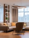Modern living room interior with soft couch and pillows near armchair and round table near window with curtains and shelves with plants near lamp