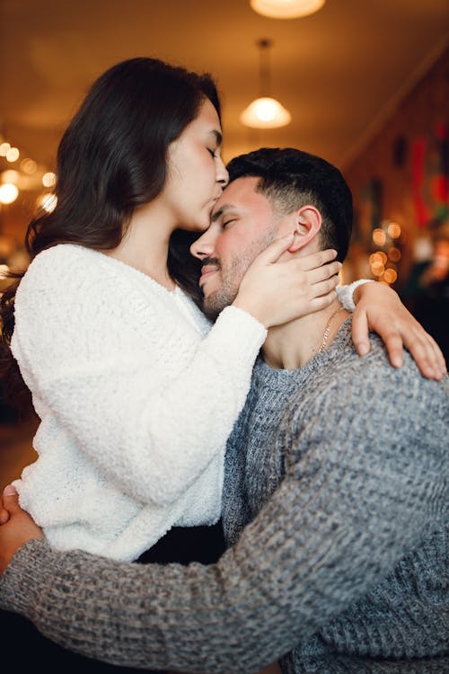 Free Side view of young couple wearing casual outfit in cafe on date and hugging tenderly while kissing head Stock Photo