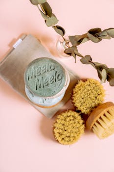 Flat lay of eco-friendly beauty products with a pink background, featuring brushes and natural soap.