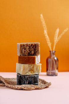 A stack of four natural handmade soaps displayed on a mat with a warm background, perfect for wellness themes.