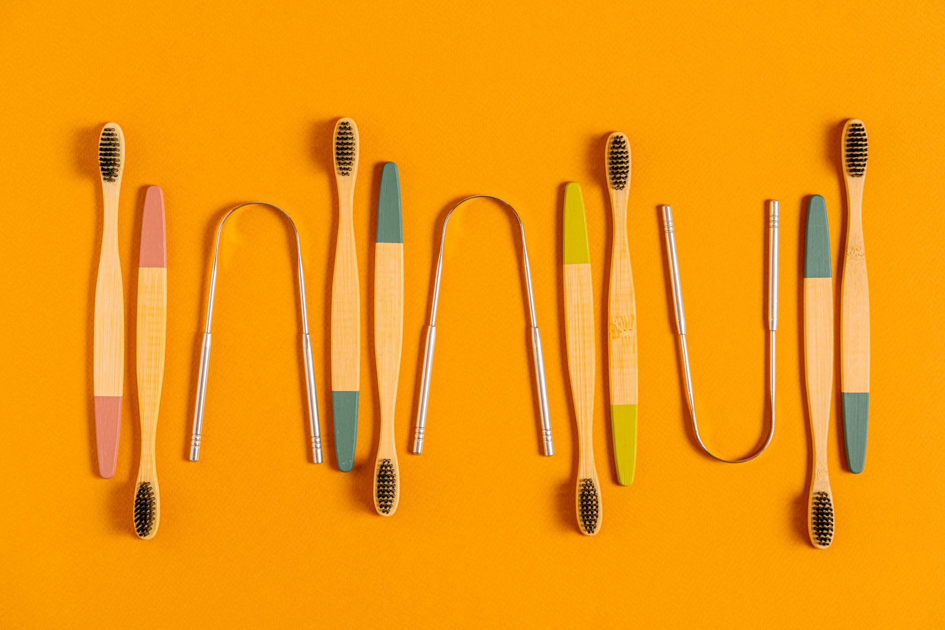 Stylish bamboo toothbrushes and tongue scrapers on a vibrant orange background, promoting sustainability.