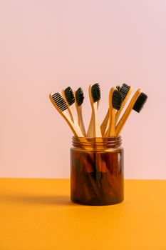 A collection of eco-friendly bamboo toothbrushes in a glass jar on a colorful background.