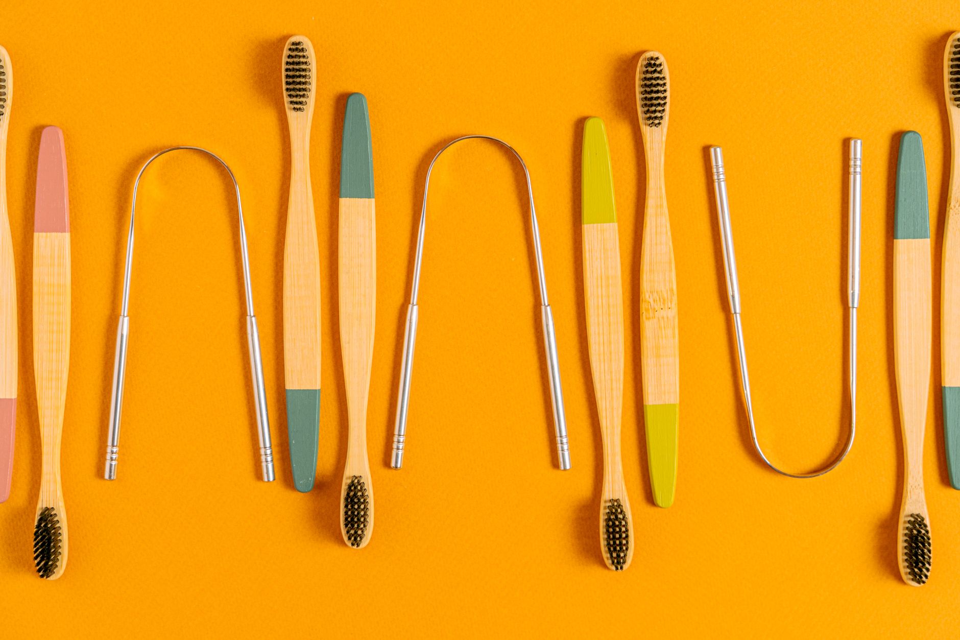 Artistic arrangement of bamboo toothbrushes and tongue scrapers on an orange surface, highlighting eco-friendly oral care.