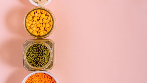 Flat lay of chickpeas, lentils, mung beans, and pumpkin seeds with pink backdrop.