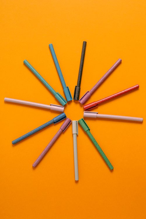 Free A vibrant top-down view of pens laid out in a circle on an orange background. Stock Photo