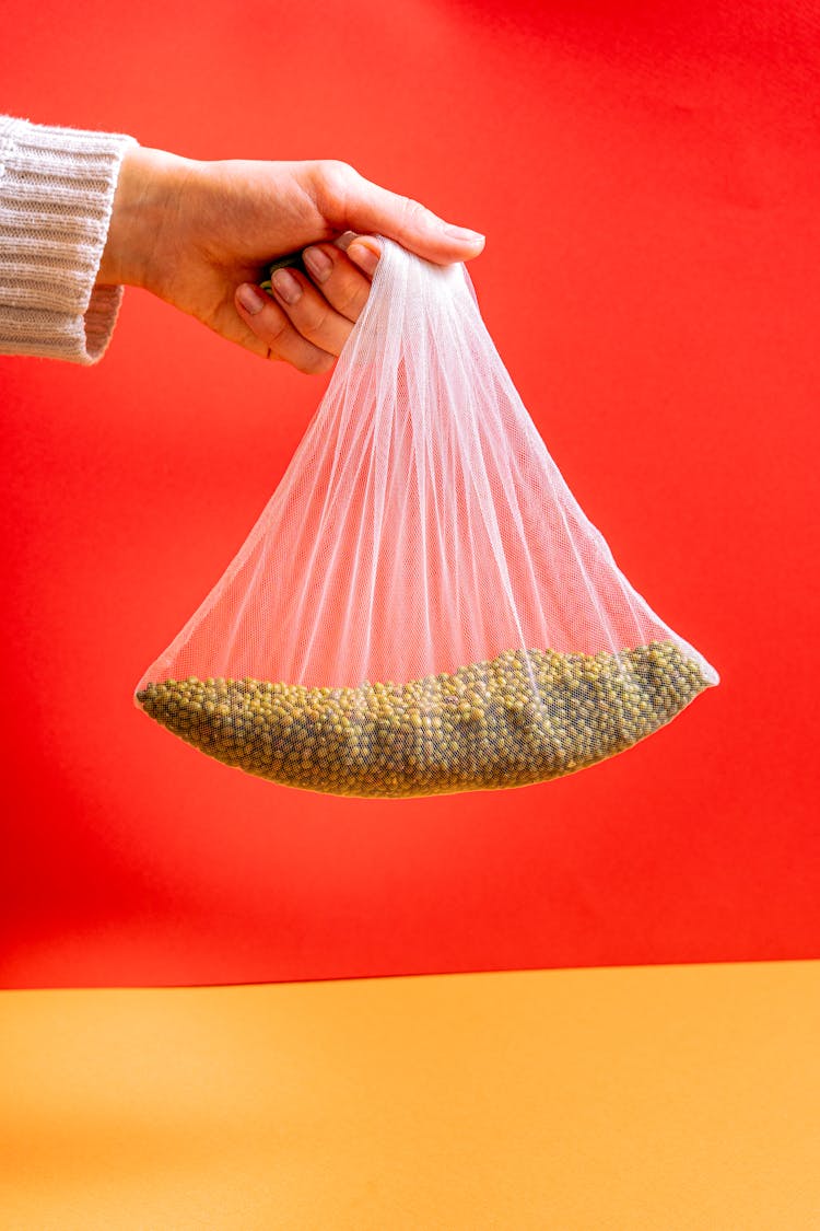 Person Holding A White Mesh Bag With Mung Beans