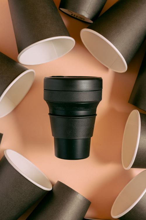Free Top view of a black collapsible coffee cup surrounded by black paper cups, highlighting eco-friendly choices. Stock Photo