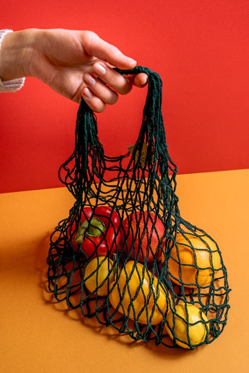 A Person Holding a Mesh Bag with Fruits and Vegetables