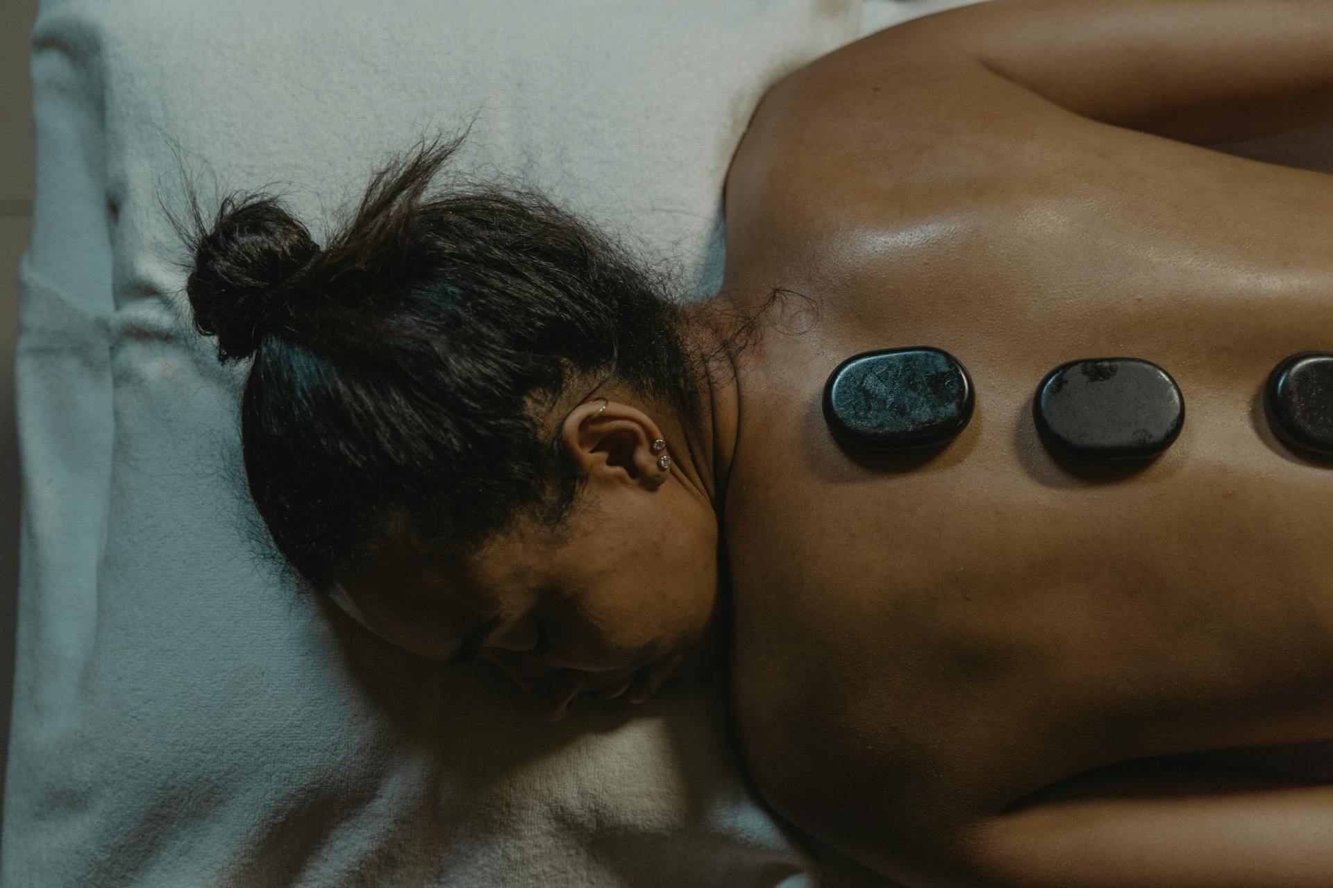 A Woman Lying on Bed with Pebbles on her Back