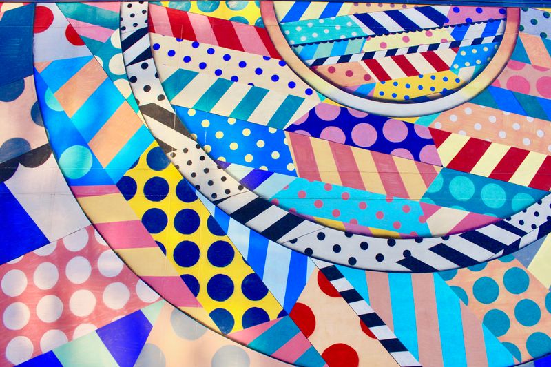 A vibrant and colorful abstract design featuring geometric patterns, stripes, and polka dots.