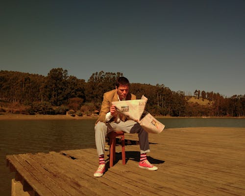 A Man Sitting on a Chair While Reading a Newspaper