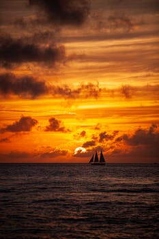 A sailboat silhouetted against a vibrant sunrise over the ocean, creating a serene and picturesque scene.