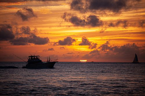 Free Stunning sunset over the ocean with boats silhouetted against a vibrant orange sky. Stock Photo