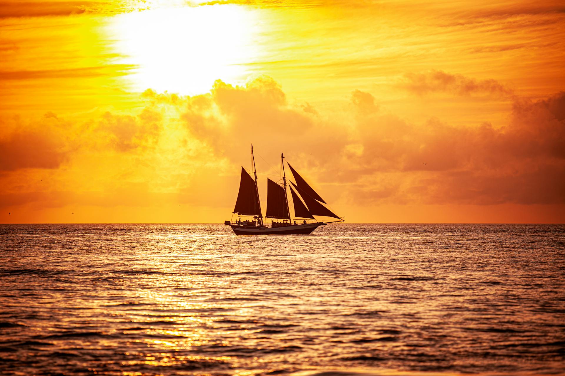Capture the beauty of a schooner sailing at sunset with golden skies.