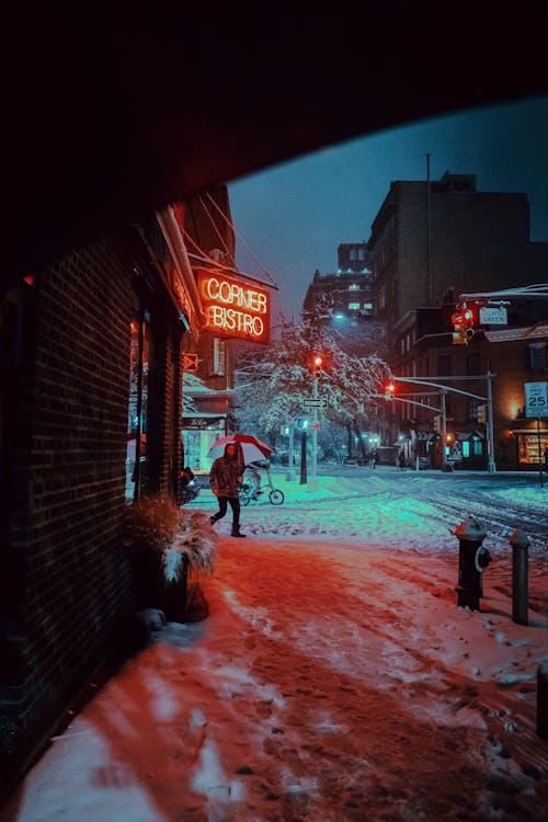 Person Walking on Snow Covered Street with an Umbrella during Night Time