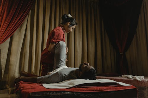 Woman in Red Shirt Stretching Lying Man's Leg in Massage Room