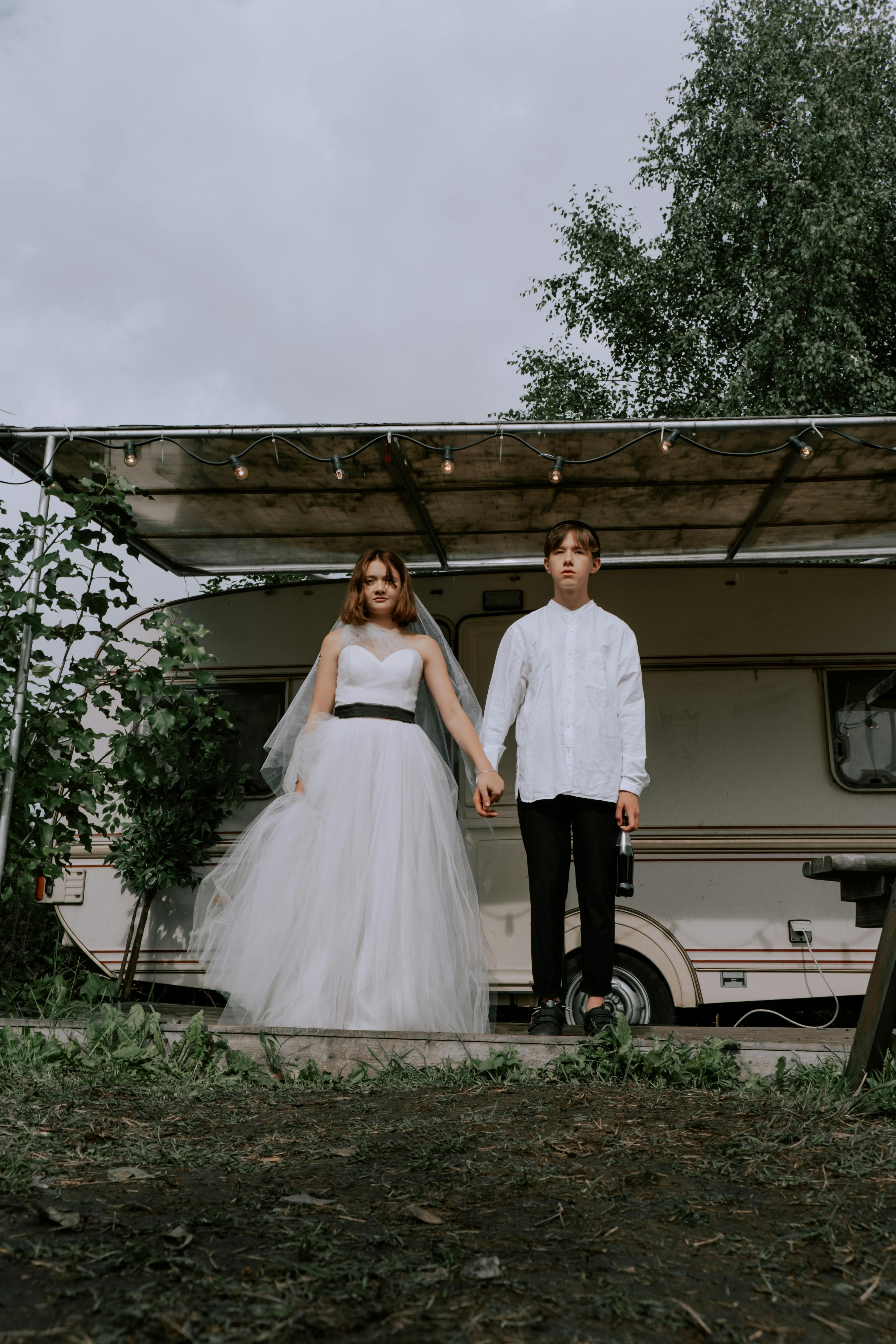 woman in white wedding gown and man in white shirt holding hands beside mobile home