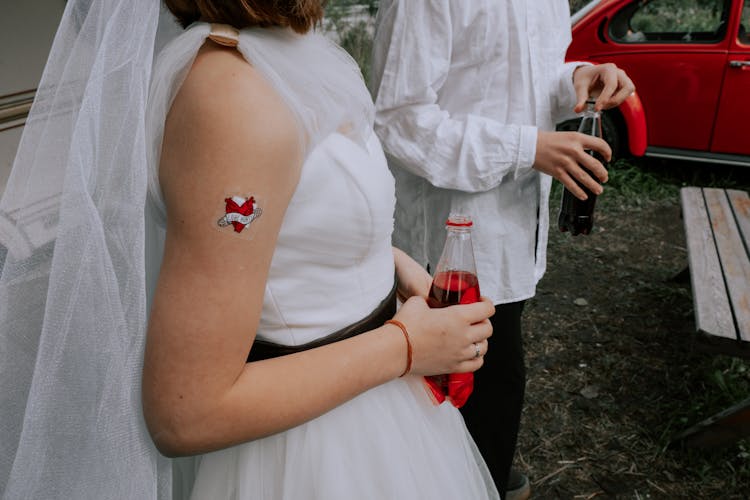 Woman In White Wedding Dress With Red Sticker On Hand Holding Lemonade Bottle