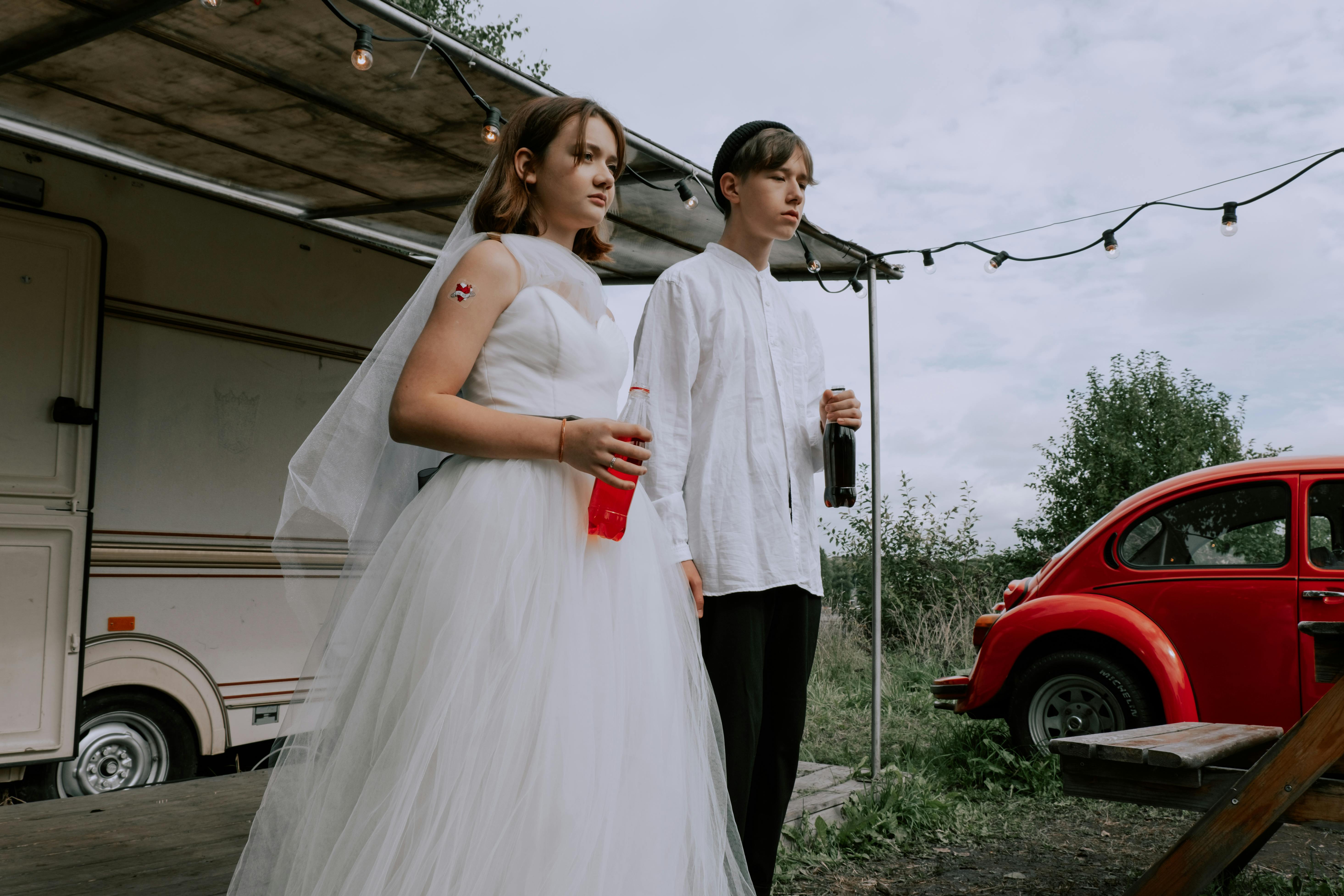 woman in white wedding dress holding red lemonade bottle while standing beside man in white shirt holding coca cola bottle