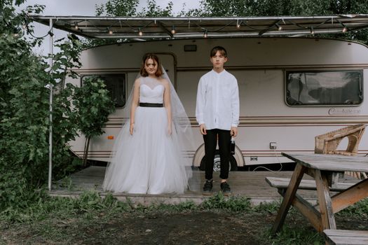 A bride and groom pose with a vintage caravan in the background, highlighting a rustic wedding theme.
