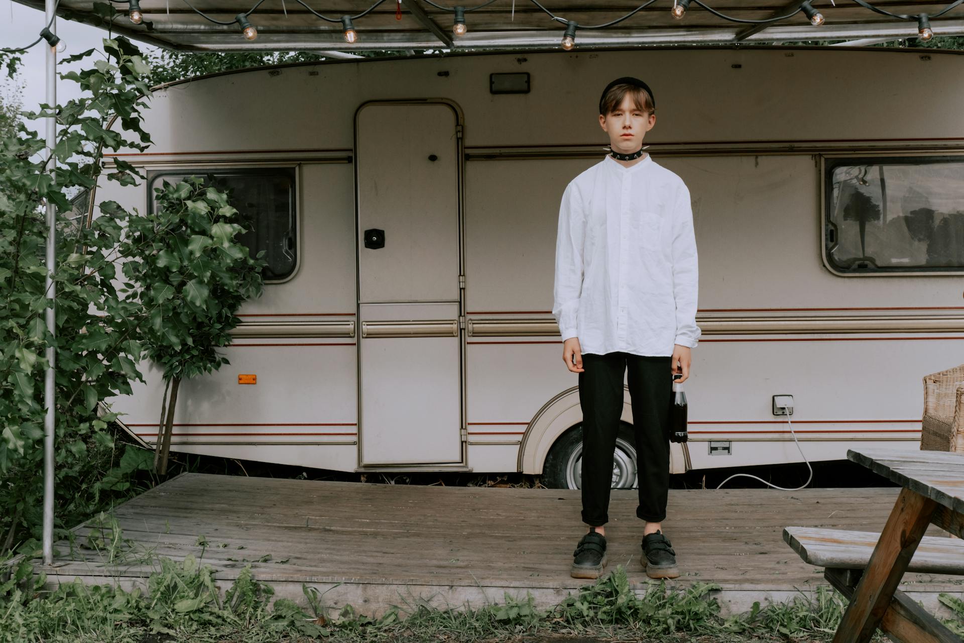 Man in White Shirt, Black Pants and Choker Standing Beside White Mobile Home