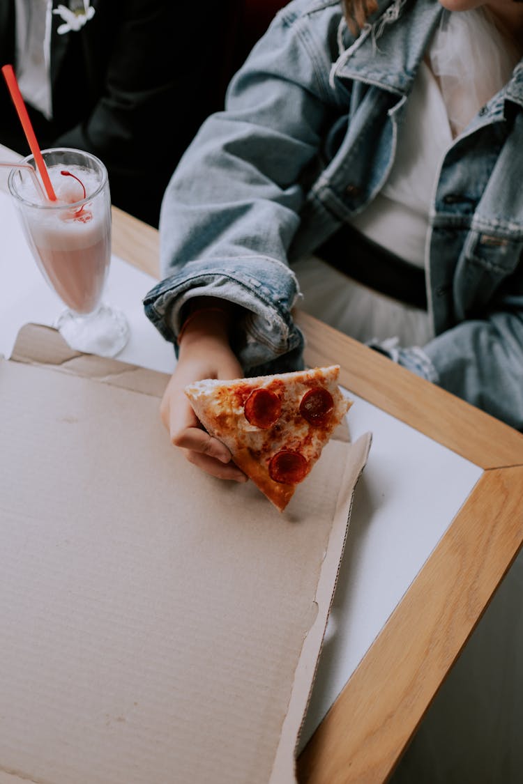 Person Holding A Slice Of Pizza