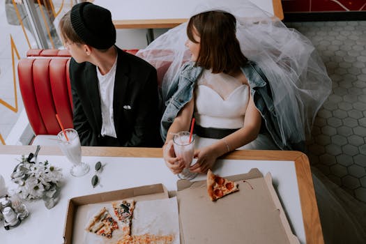 Quirky wedding photo of a bride and groom enjoying pizza and milkshakes in a retro diner.