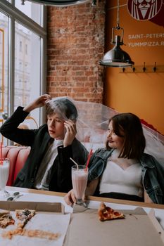 A bride and groom share a fun moment with milkshakes and pizza in a cozy diner setting.