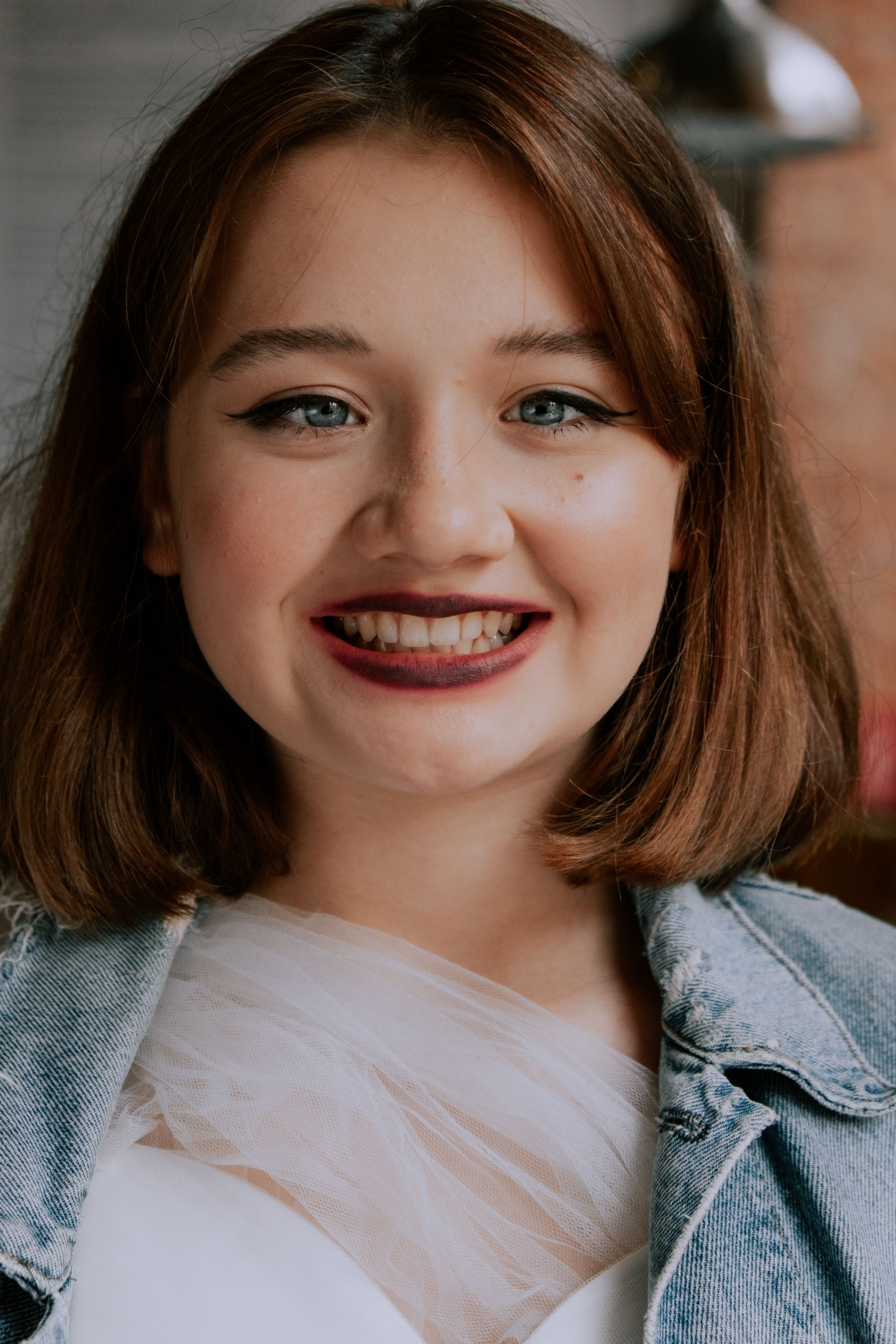 Cheerful portrait of a young woman smiling, wearing a denim jacket indoors.