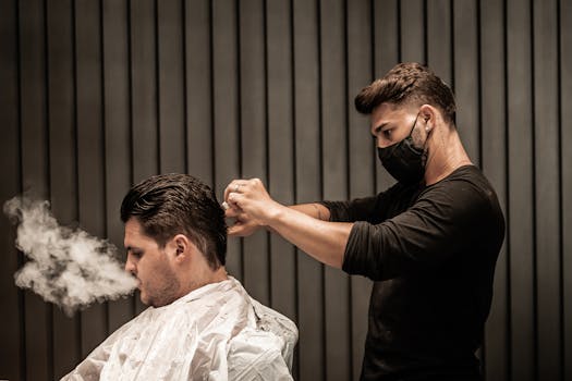 A barber wearing a mask trims a customer's hair while the customer exhales smoke indoors.