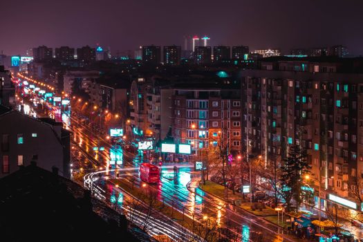 A vibrant aerial view of Skopje's city lights reflecting on wet streets at night.