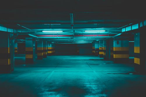 Free Moody underground parking garage with dramatic neon lighting casting a teal glow. Stock Photo