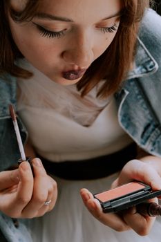 Close-up of a woman applying lipstick and blush, showcasing beauty and self-care.