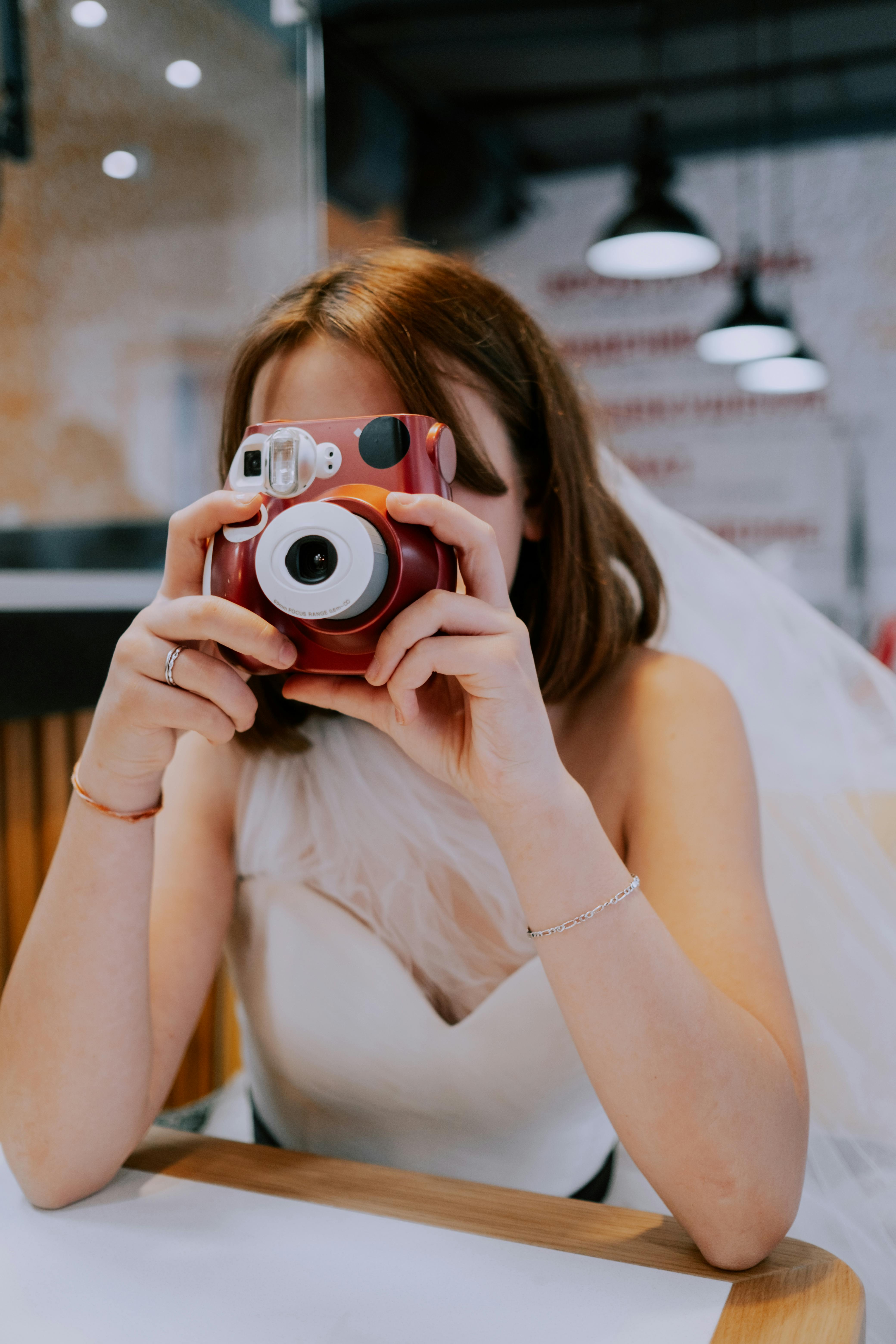 Bride in a wedding dress using an instant camera indoors. Perfect shot for capturing memories.